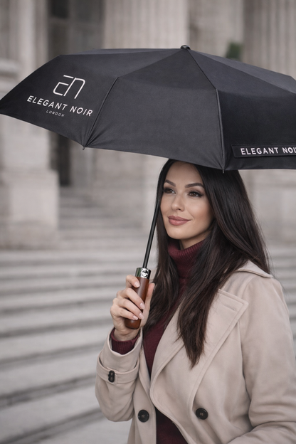 Woman holding a black umbrella with 'Elegant Noir' branding in front of classical architecture.